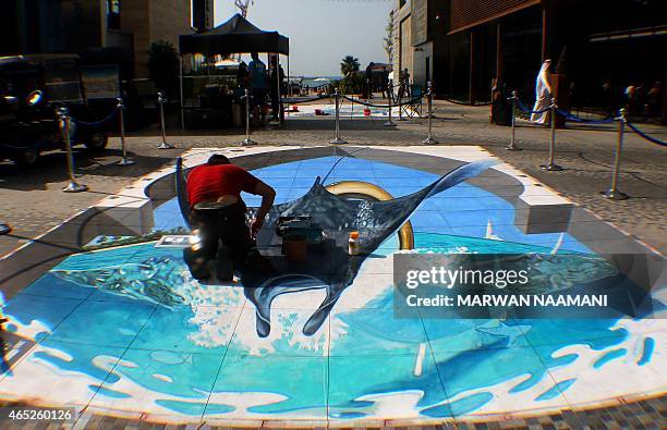 Picture taken though a magnifying lens shows an artist working on his chalk 3-D artwork on March 4, 2015 near the Jumeirah Beach Residence in Dubai...
