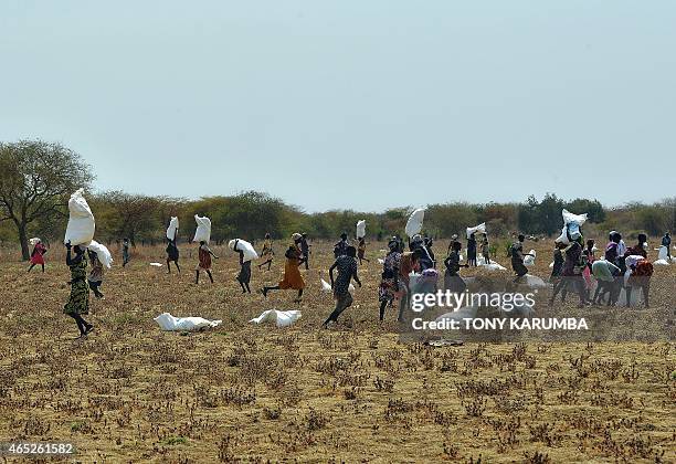 Villagers carry sacks of food aid in a field following an air-drop on February 24, 2015 at a village in Nyal, Panyijar county, near the northern...