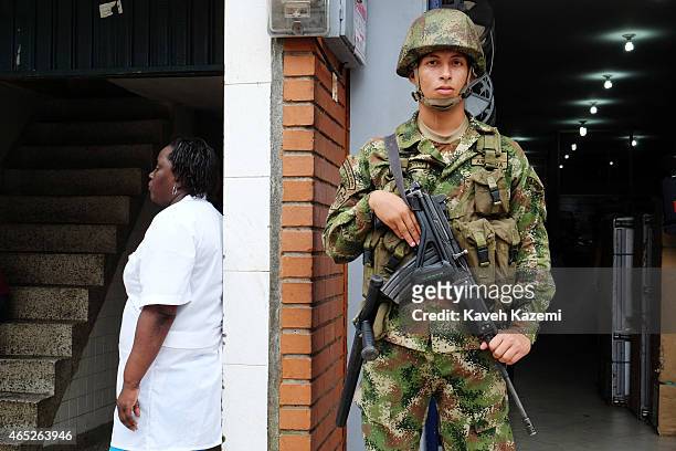 An armed marine from the navy infantry stands next to a womanat the entrance of a fish shop in La Galeria neighborhood on January 15, 2015 in...