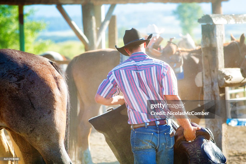 Rear view of cowboy carrying riding equipment
