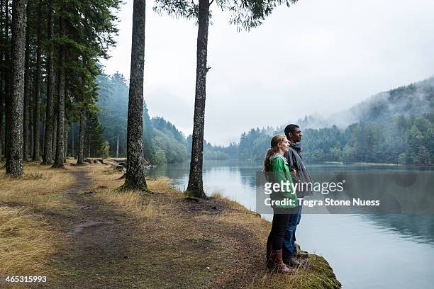 young couple looks out over a misty lake. - raincoat stockfoto's en -beelden