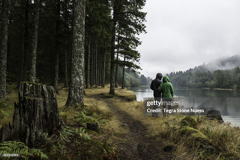 Couple looks out over a misty lake in a forest.