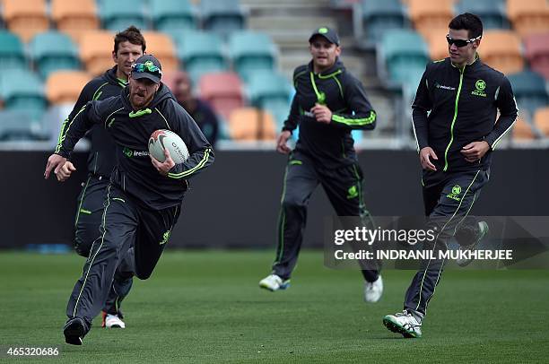 Ireland cricketer John Mooney , watched by teammates Gary Wilson , William Porterfield and George Dockrell , runs with a rugby ball during a training...