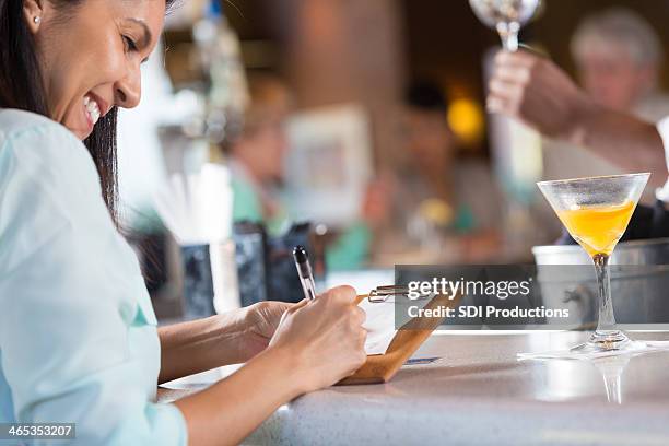 woman signing receipt after paying bar tab in restaurant - bar drink receipt stock pictures, royalty-free photos & images