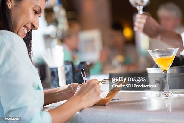 woman signing receipt after paying bar tab in restaurant - gratuity stock pictures, royalty-free photos & images