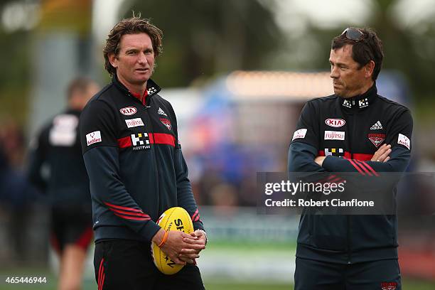 Bombers coach James Hird speaks with assistant coach Mark Harvey during the warm up for the NAB Challenge AFL match between the Essendon Bombers and...