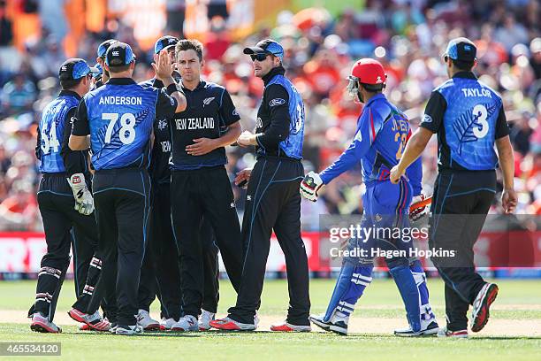 Trent Boult of New Zealand is congratulated by teammate Corey Anderson after taking the wicket of Javed Ahmadi of Afghanistan while Usman Ghani looks...