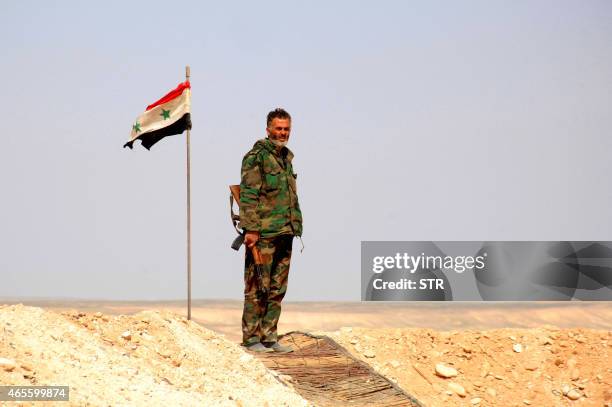 Member of the Syrian government forces stands at a look out point next to his national flag after they retook the village of Jihar and the...