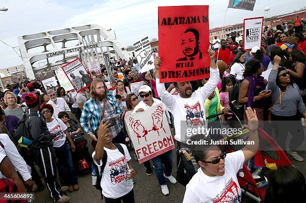 Marchers carry signs as they walk across the Edmund Pettus Bridge during the 50th anniversary commemoration of the Selma to Montgomery civil rights...