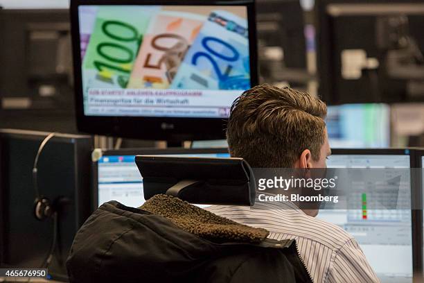 Financial trader monitors data on computer screens as a desktop television shows euro currency banknotes at the Frankfurt Stock Exchange in...