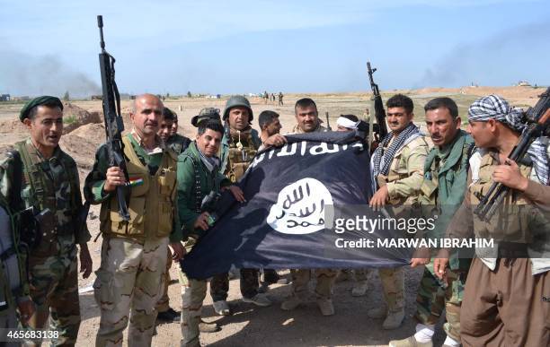Iraqi Kurdish Peshmerga fighters pose for a photo holding an Islamic State group flag in the village of Sultan Mari west of the city of Kirkuk on...