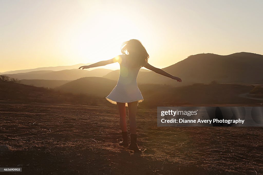 Teen girl spinning in field at sunset