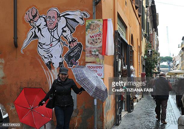 Woman poses in front of a street art mural showing Pope Francis as a superman, flying through the air with his white papal cloak billowing out behind...