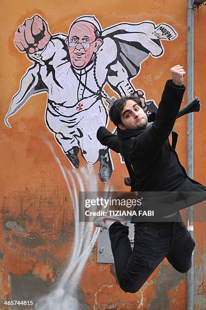 Tourist jumps for a picture in front of a street art mural showing Pope Francis as a superman, flying through the air with his white papal cloak...