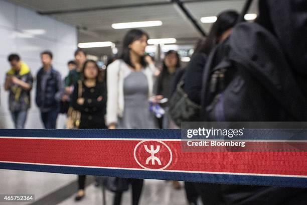 Boundary tape displays the MTR Corp. Logo as commuters walk inside HKU Station in Hong Kong, China, on Monday, March 9, 2015. MTR, Hong Kong's...