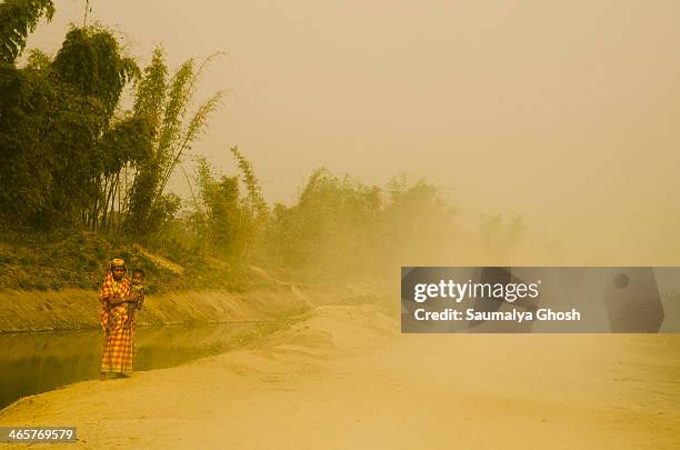 Mother and child are standing on a village road in a dusty and foggy winter morning.