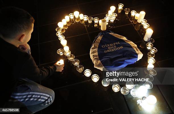 Boy lays a candles to form a heart around a bag reading "Nice Olympic Swimming" during a candlelight vigil for swimming gold medallist Camille Muffat...