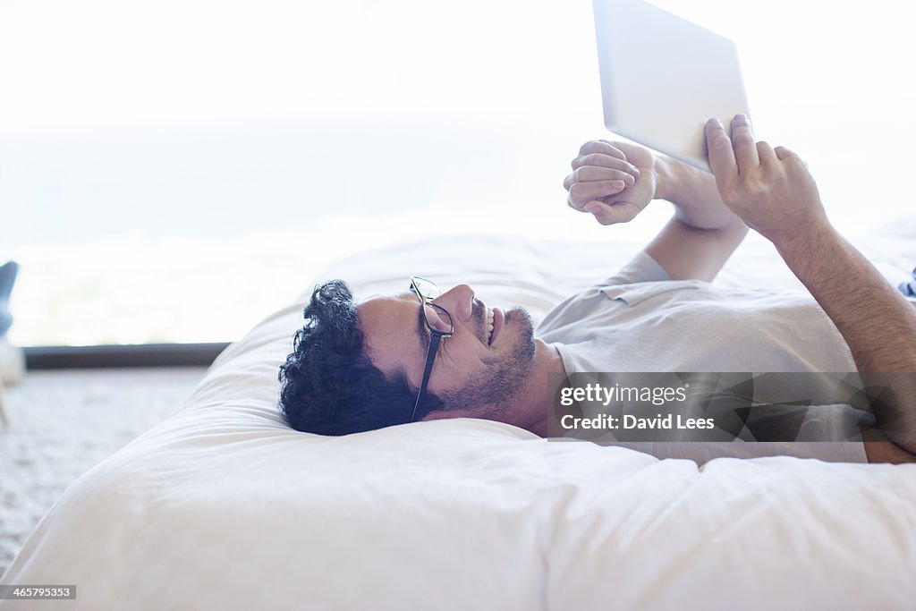 Man laying on bed using digital tablet