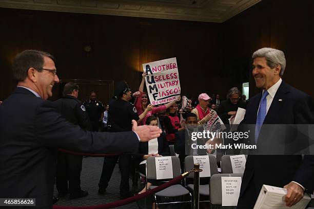 Protesters from Code Pink hold up signs as Secretary of State John Kerry and Defense Secretary Ashton Carter arrive to testify to the Senate Foreign...