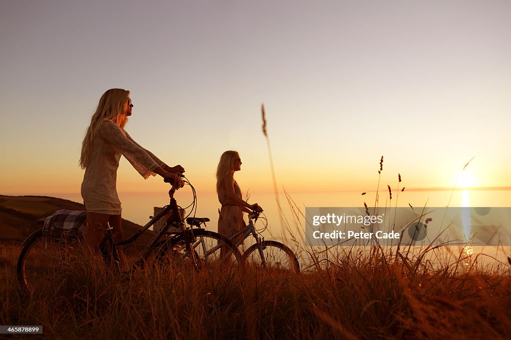 Two girls with bikes watching sunset over sea