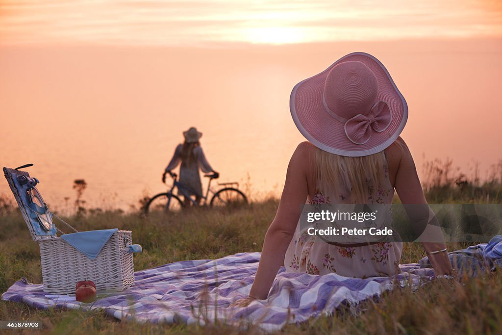 Two women on coastal cliff with picnic and bikes