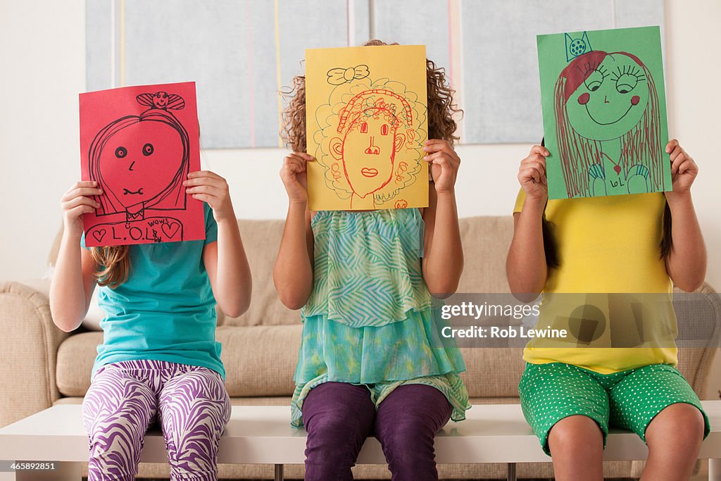 Three girls holding pictures over faces