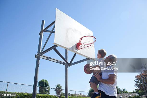 man lifting grandson to basketball hoop - grandparents raising grandchildren stock pictures, royalty-free photos & images