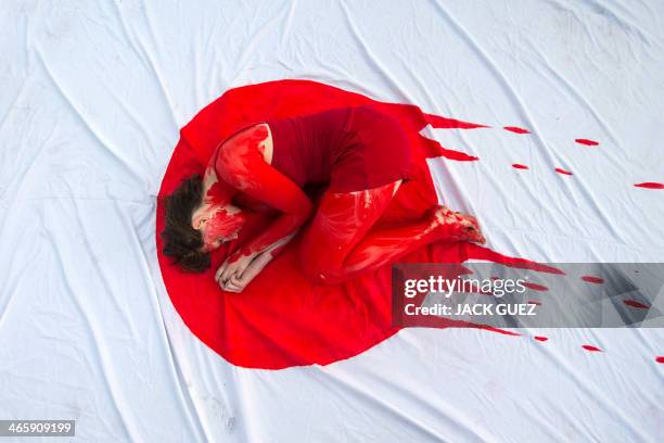 An Israeli member of the "Taiji Dolphin Action Group", with a red body painting to evok blood, is curled up on a sheet depicting the Japanese flag,...