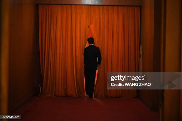 Security guard watches through the curtain during the 3rd plenary session of the third session of the 12th National People's Congress at the Great...