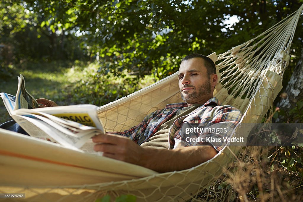 Man lies in hammock reading the paper