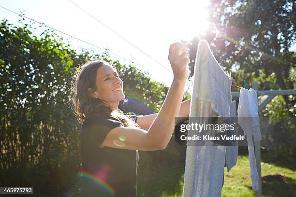 woman hanging up laundry in her garden at sunset - airing stockfoto's en -beelden