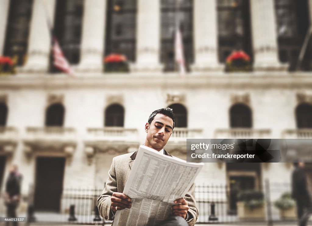 Business man reading a newspaper sitting on wall street