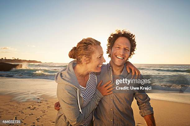 couple embracing and smiling by the sea - couple sand sunset stock pictures, royalty-free photos & images