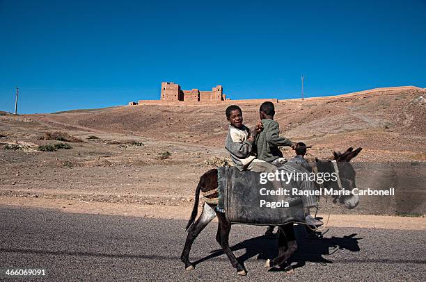 Little boys on a donkey passing by a beautiful ancient adobe Kasbah.