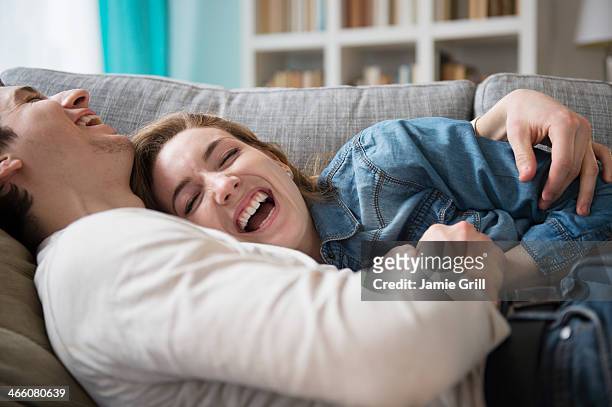 couple laughing together on couch - verliefd worden stockfoto's en -beelden