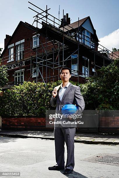 man wearing suit, holding hard hat, standing outside house with scaffolding - cultura orientale photos et images de collection