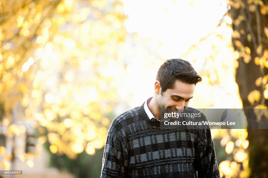 Young man looking down in sunlit park, smiling