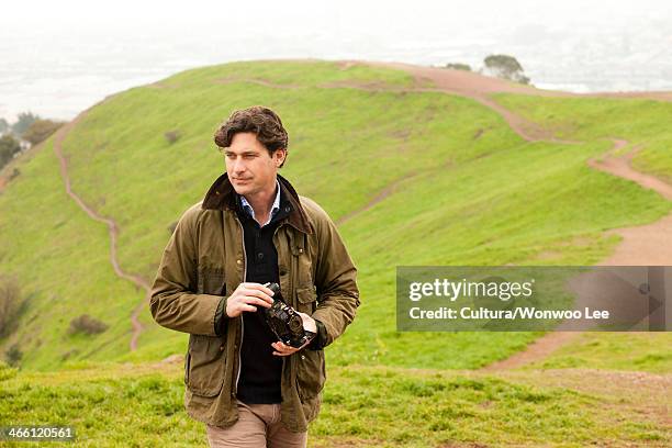 mid adult man holding vintage camera in countryside, looking away - waxed jacket stock pictures, royalty-free photos & images