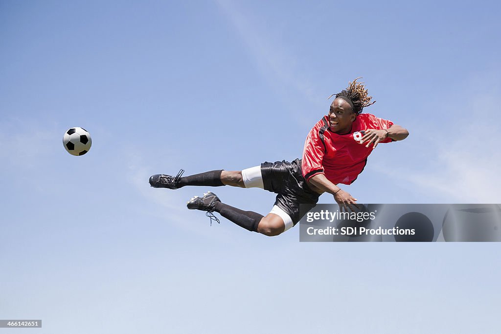 Adult soccer player kicking ball in mid-air during game