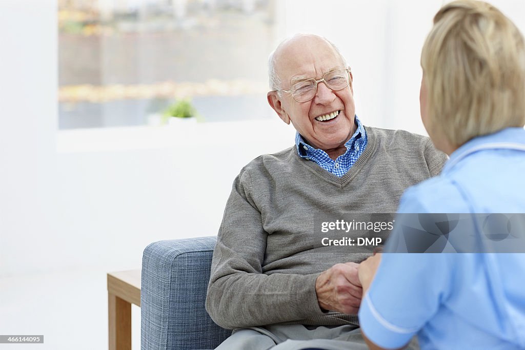 Happy elderly patient talking with nurse at home