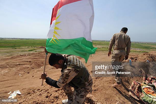 Peshmerga fighter plants a Kurdish flag atop a new earth berm position as Iraqi Kurdish forces push the frontline forward against ISIS forces in the...