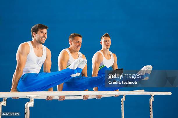 three young gymnasts posing on the parallel bars - artistic gymnastics stock pictures, royalty-free photos & images