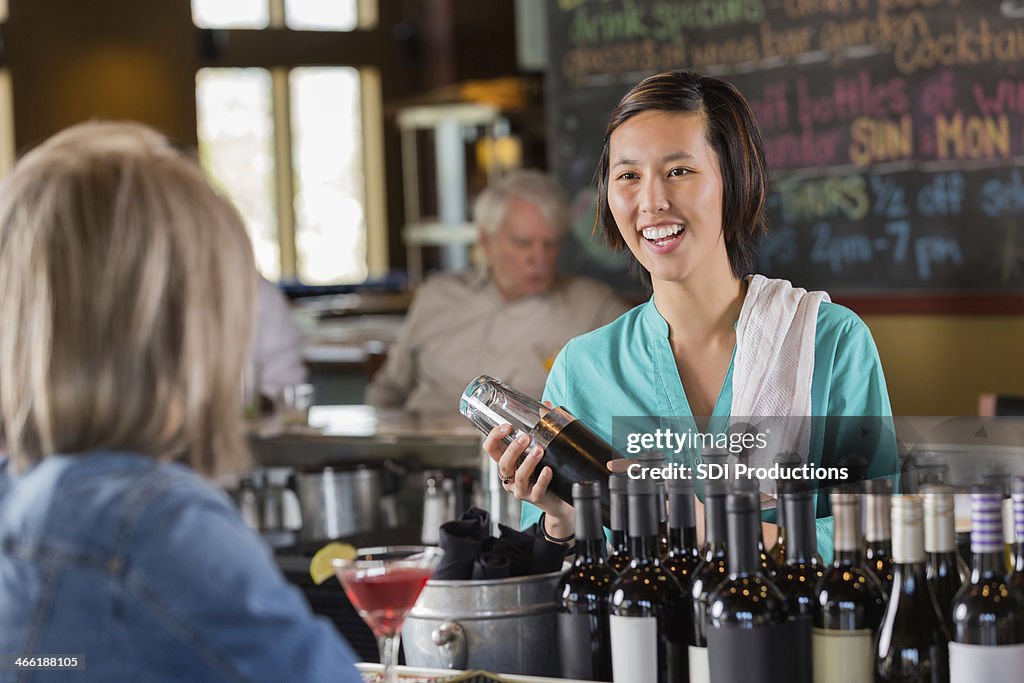 Asian bartender making mixed drink while talking to restaurant customer