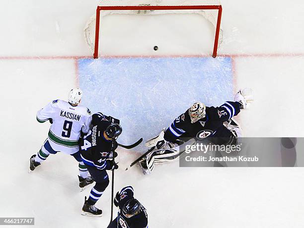 Zack Kassian of the Vancouver Canucks and Zach Bogosian of the Winnipeg Jets watch as the puck goes into the net behind goaltender Ondrej Pavelec for...