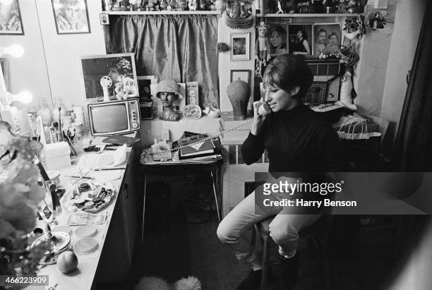American actress and singer Barbra Streisand makes a phone call from her dressing room, 6th October 1965. On the wall are portraits of her husband,...