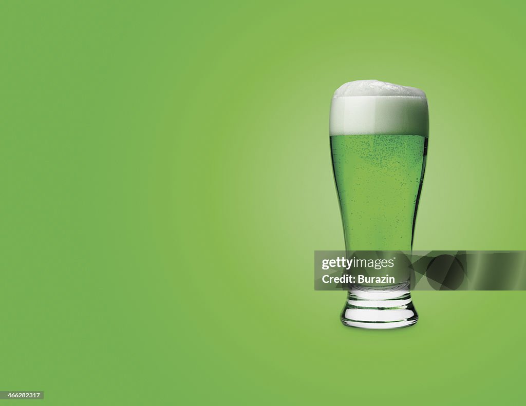 Glass of green beer on colored background