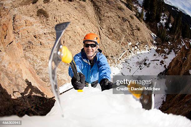 man smiling and climbing a frozen waterfall. - icepick stock pictures, royalty-free photos & images