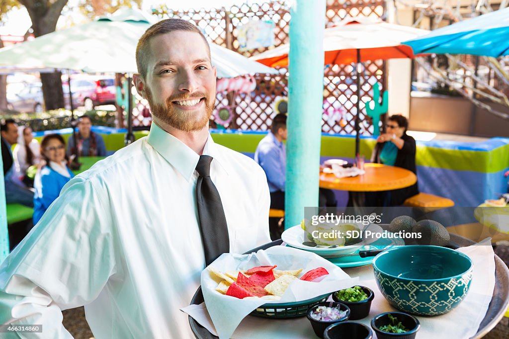 Waiter at Tex-Mex restaurant serving chips to customers on patio