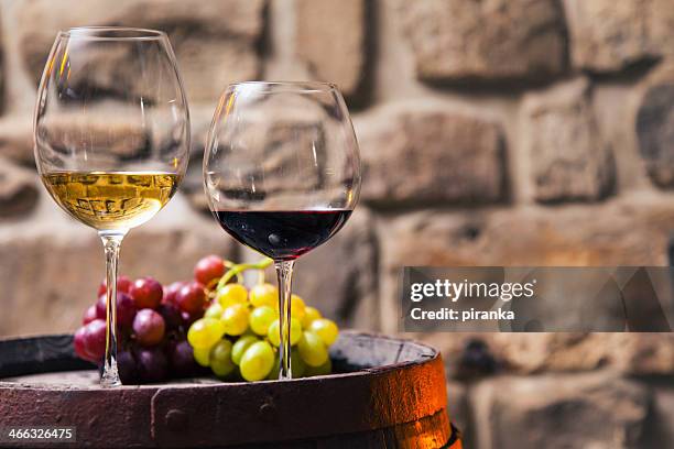 two glasses of red and white wine in the cellar with grapes - red grape stockfoto's en -beelden