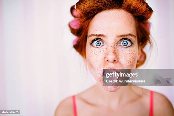 young redhead woman with curlers in hair blows bubble - hair curlers stock pictures, royalty-free photos & images